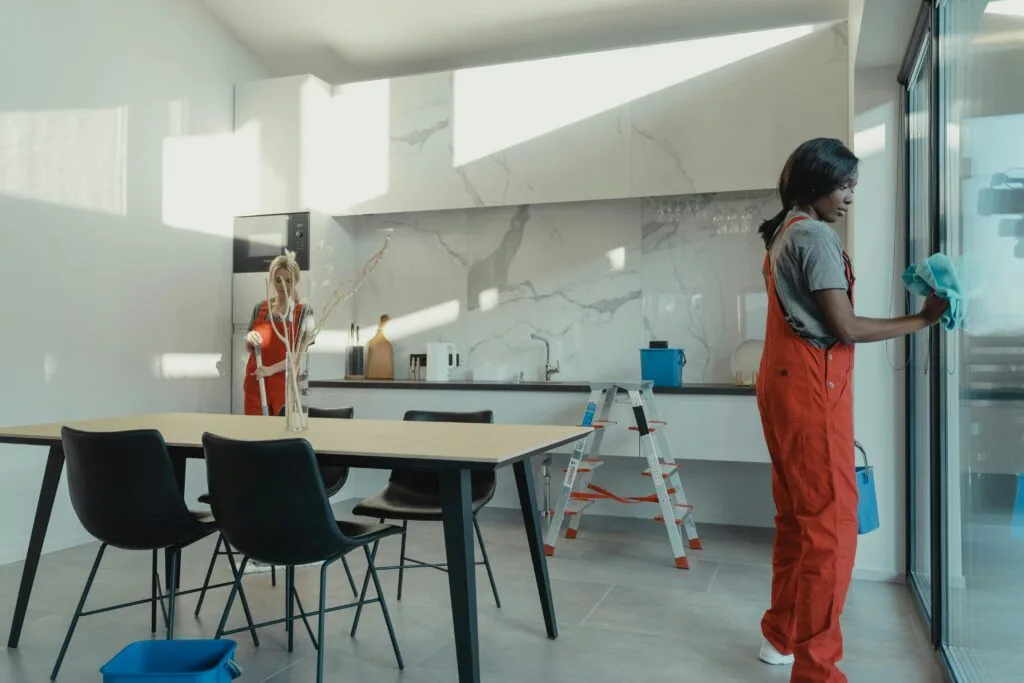 Dos empleadas de limpieza con mono naranja trabajando en una vivienda reformada, luminosa