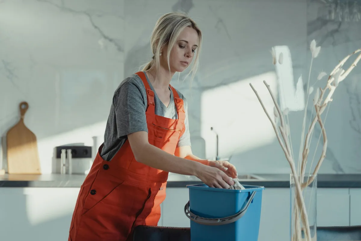 Persona con mono de trabajo naranja limpiando una cocina reformada, con un cubo de fregar