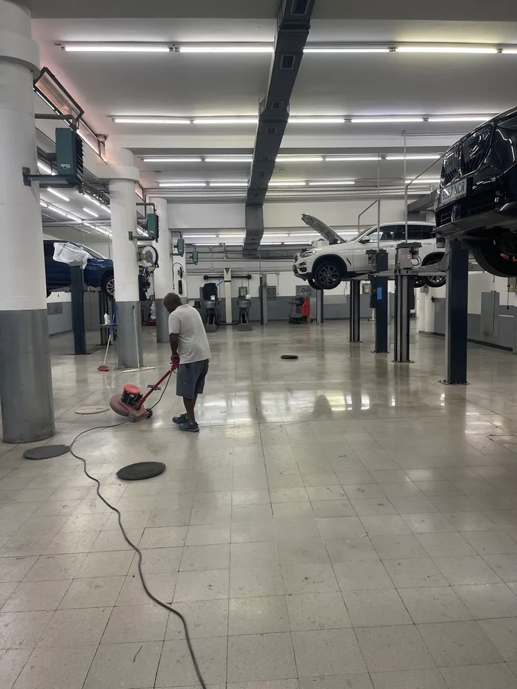 Empleado de Servicios24 puliendo el suelo del taller de BMW Lleida junto a un vehículo elevado