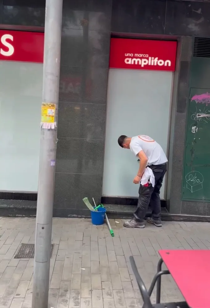 Empleado de Servicios24 limpiando el cristal exterior de la tienda GAES, junto al cartel de Amplifon