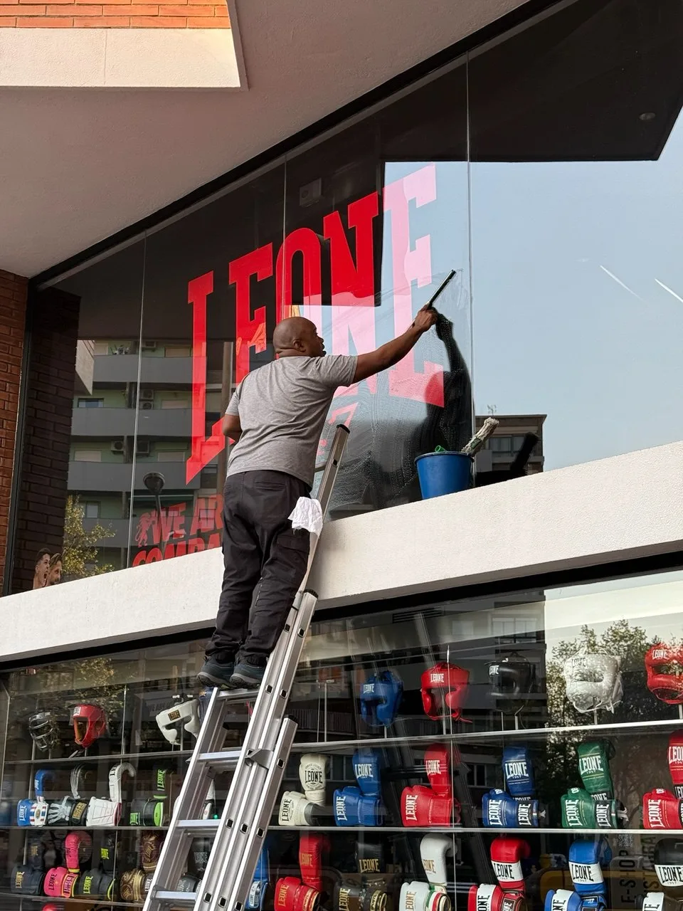 Empleado de Servicios24 subido a una escalera limpiando el cristal de la fachada de la tienda Leone en Barcelona