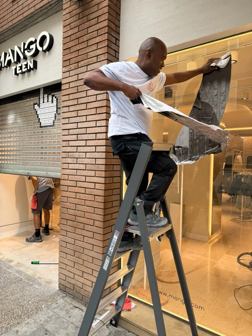 Empleado de Servicios24 limpiando el rótulo y la persiana de una tienda Mango antes de su apertura
